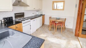 A compact kitchen with white cabinets, a stove, a microwave, and a dining area with wooden chairs and a table.