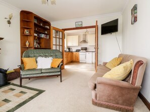 A living room with a green sofa, a brown sofa, a wooden bookshelf, and a kitchen in the background. - Saoirse (Gortmore)