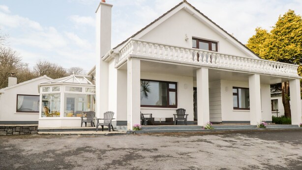 A white two-story house with a covered porch, a conservatory, and outdoor seating.