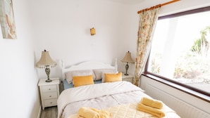 Een slaapkamer met een bed, twee nachtkastjes, een raam met gordijnen en een wandlamp.