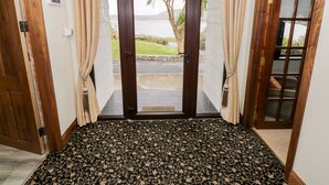 Een kamer met een grote houten deur die uitkomt op een balkon met uitzicht op een strand en palmbomen.