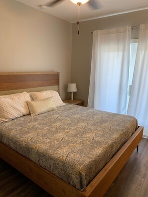 A bedroom with a wooden headboard, a patterned bedspread, two pillows, a bedside lamp, and a window with curtains. - On 30A, walk to 2 beaches, 1 King bed/attached bathroom, pool, gym (Santa Rosa Beach)