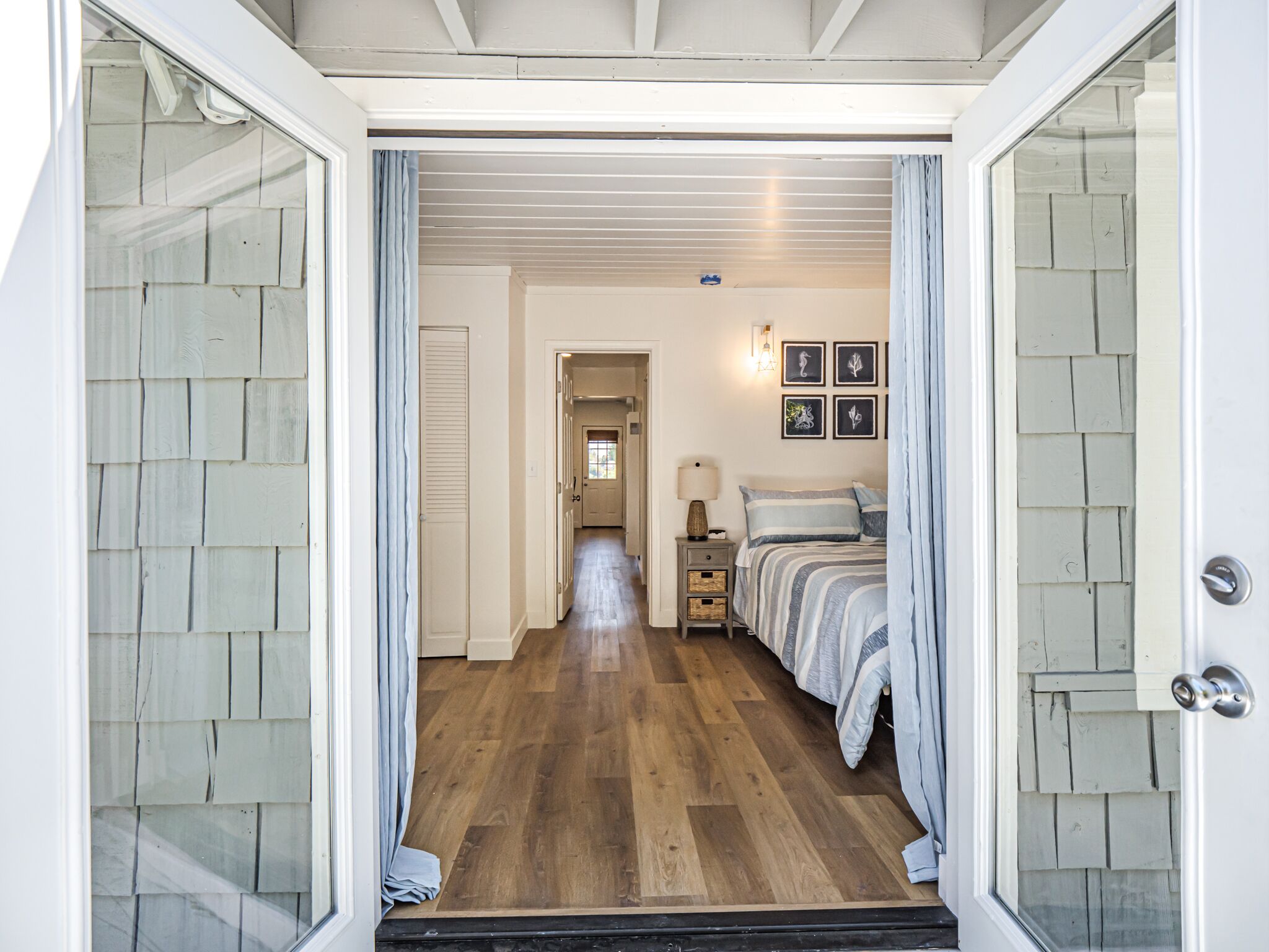 A hallway leading to a bedroom with a bed, bedside tables, and framed artwork on the wall.