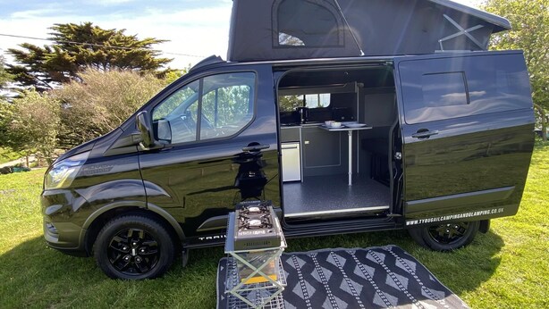 A black van with a kitchen area, a small table, and a sleeping area. - Inviting 2 bed Camper in Holyhead (Holyhead)