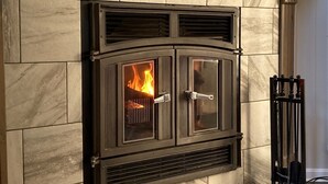 A stone fireplace with a glass door, a metal grate, and a fire burning inside. - Simple Pleasures-Woods Golf Resort-Peaceful & Calm (Hedgesville)