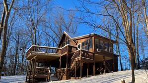 A wooden cabin with multiple levels and a deck, surrounded by trees and snow. - Simple Pleasures-Woods Golf Resort-Peaceful & Calm (Hedgesville)