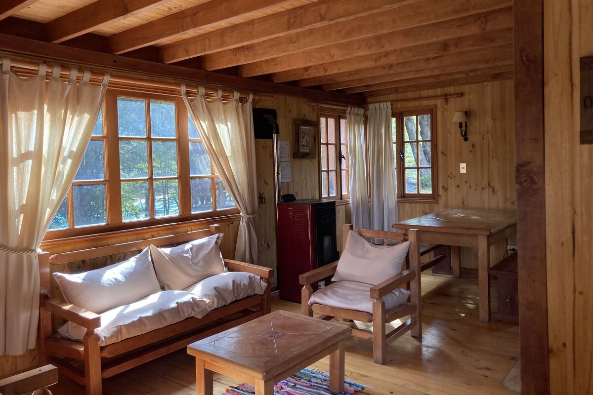 A wooden cabin interior with a sofa, chairs, a table, and a fireplace.