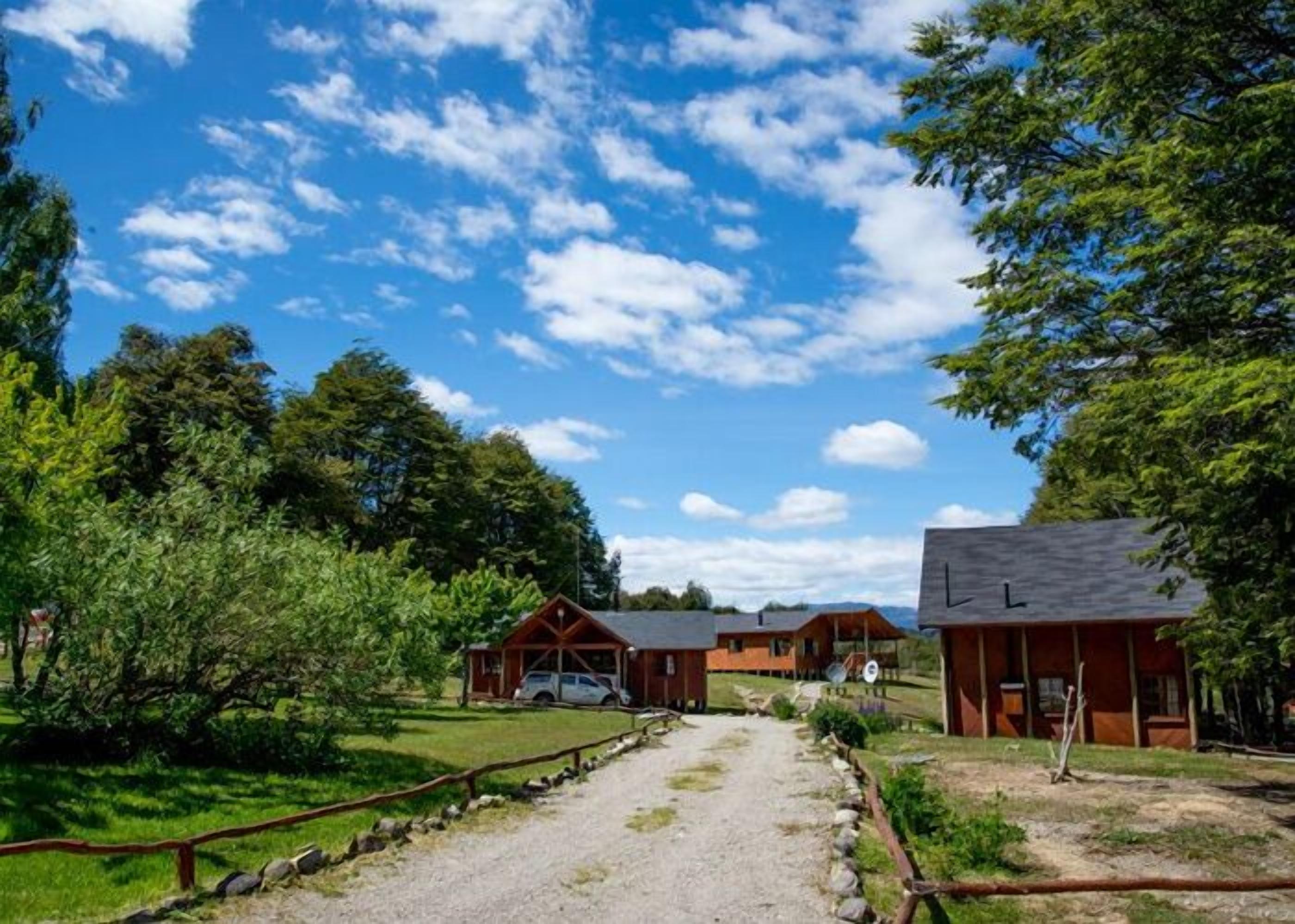 A rural lodge with wooden cabins, a gravel path, and surrounding greenery.