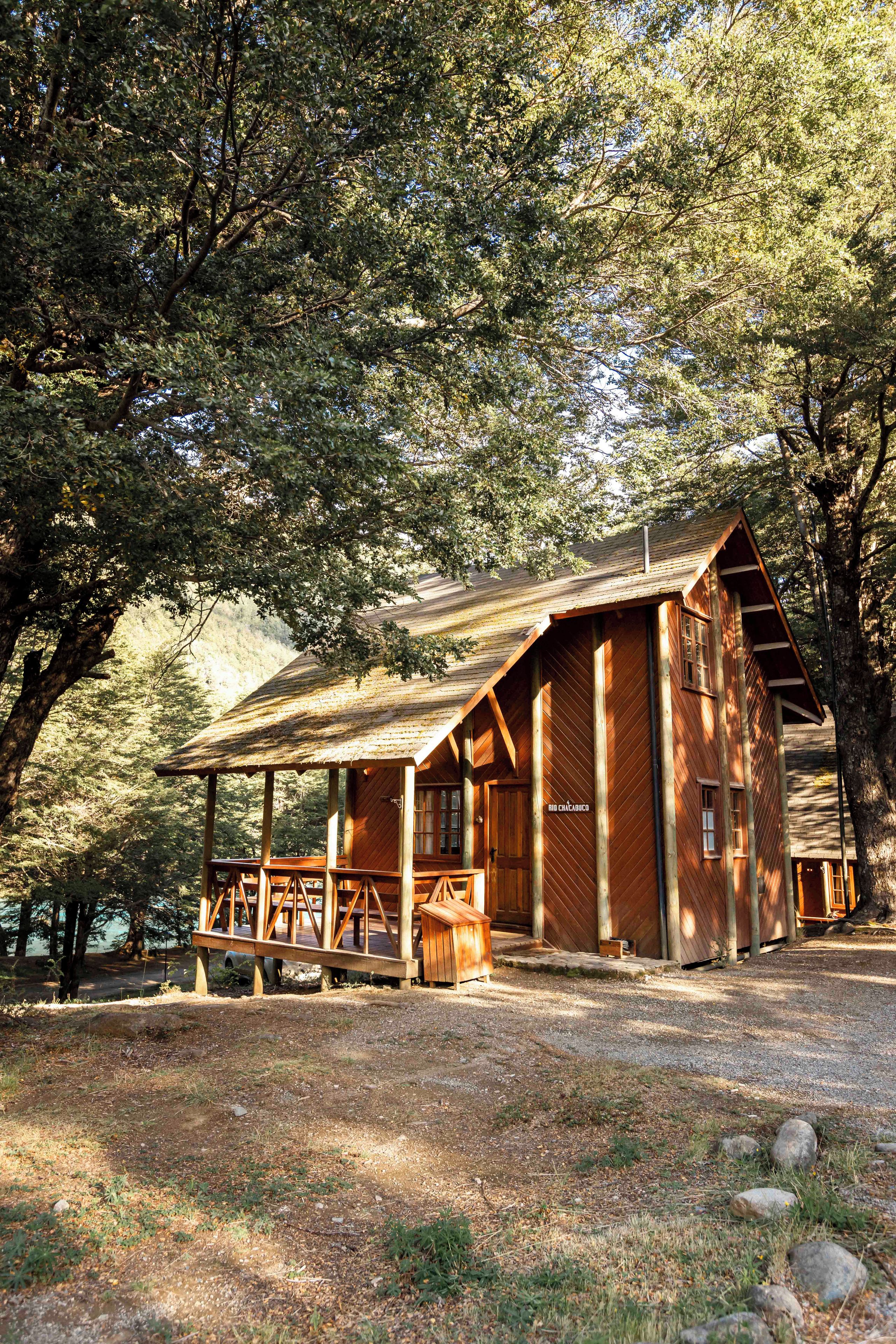 A rustic wooden cabin with a porch, surrounded by trees.