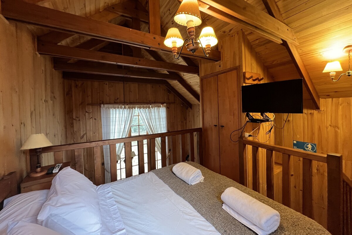 Een houten kamer met een bed, een aan de muur bevestigde televisie en een raam met gordijnen.