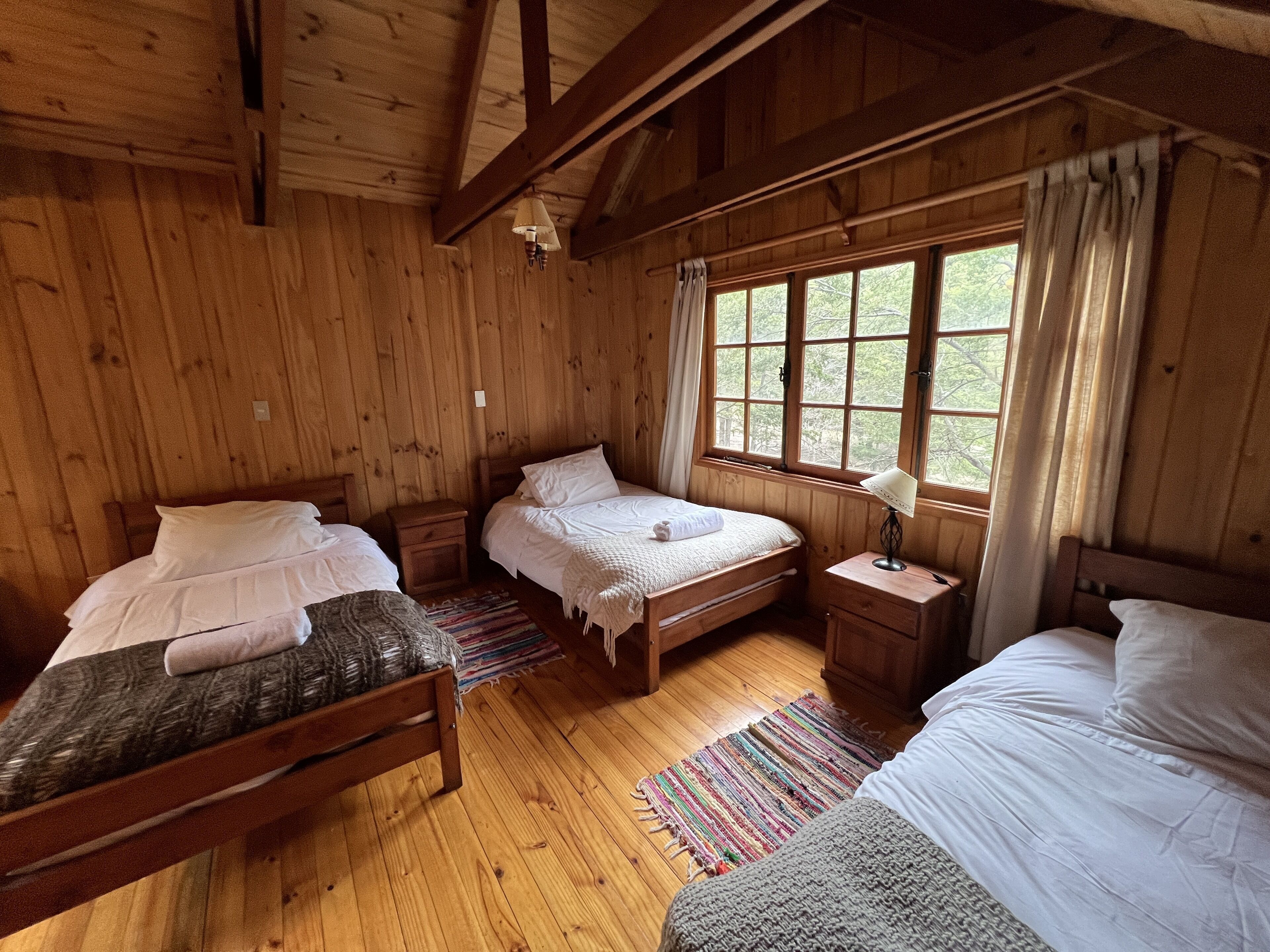 Una habitación de cabaña de madera con dos camas, una mesita de noche y un ventanal con cortinas.
