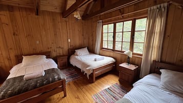 Una habitación de cabaña de madera con dos camas, una mesita de noche y un ventanal con cortinas.