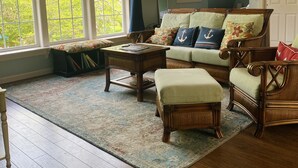 Una sala de estar acogedora con piso de madera, un ventanal grande, un sofá con cojines estampados y una mesa de centro.