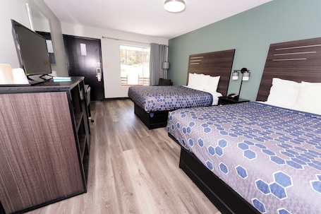 A hotel room with two beds, a desk, a chair, a TV, and a door.