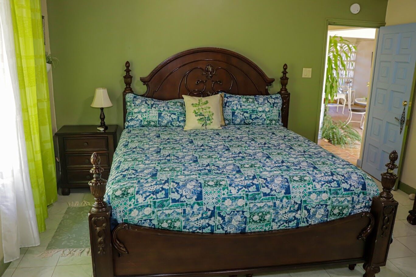A bedroom with a wooden bed, green walls, and a small bedside table with a lamp.
