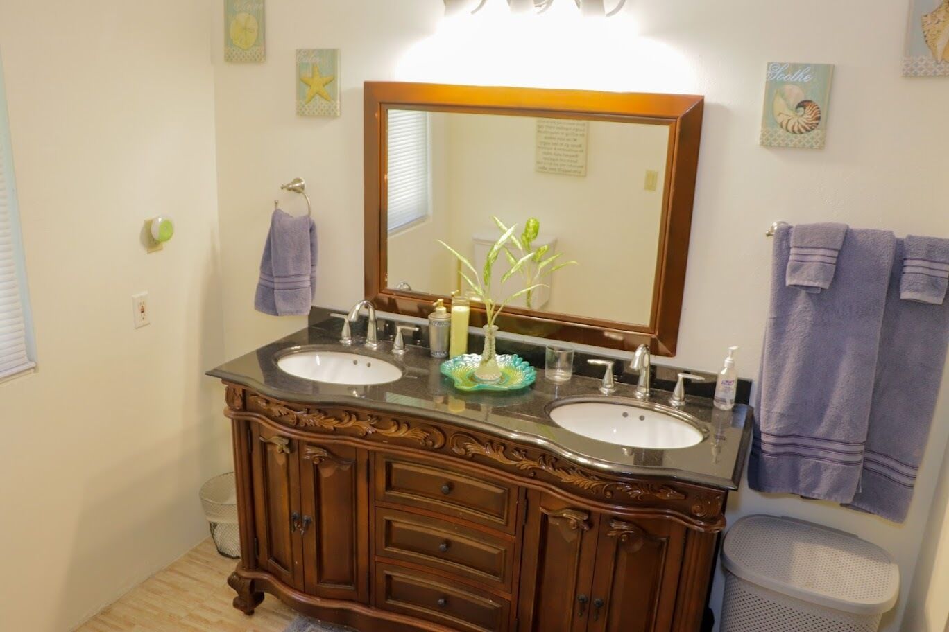 Casa de banho com duas pias, um espelho grande e decoração na parede.