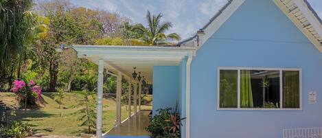 A light blue building with a covered porch and a pool in front.