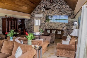 Un salon chaleureux aux murs en pierre, au plafond en bois et à la grande fenêtre donnant sur un paysage magnifique.
