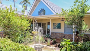 A house with a blue roof, a fountain, and tropical plants. - Seven Palms Villa  (Runaway Bay)