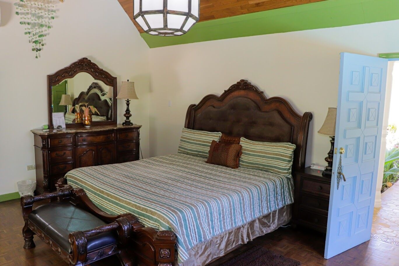 A bedroom with a large bed, a wooden dresser, a mirror, and a door.