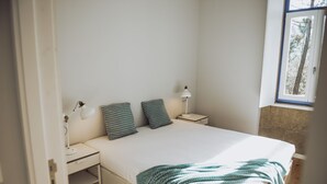 A bedroom with a bed, two bedside tables, a nightstand, a window, and a door.