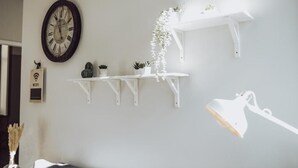 A room with a wall-mounted clock, white shelves with plants, and a hanging light fixture.