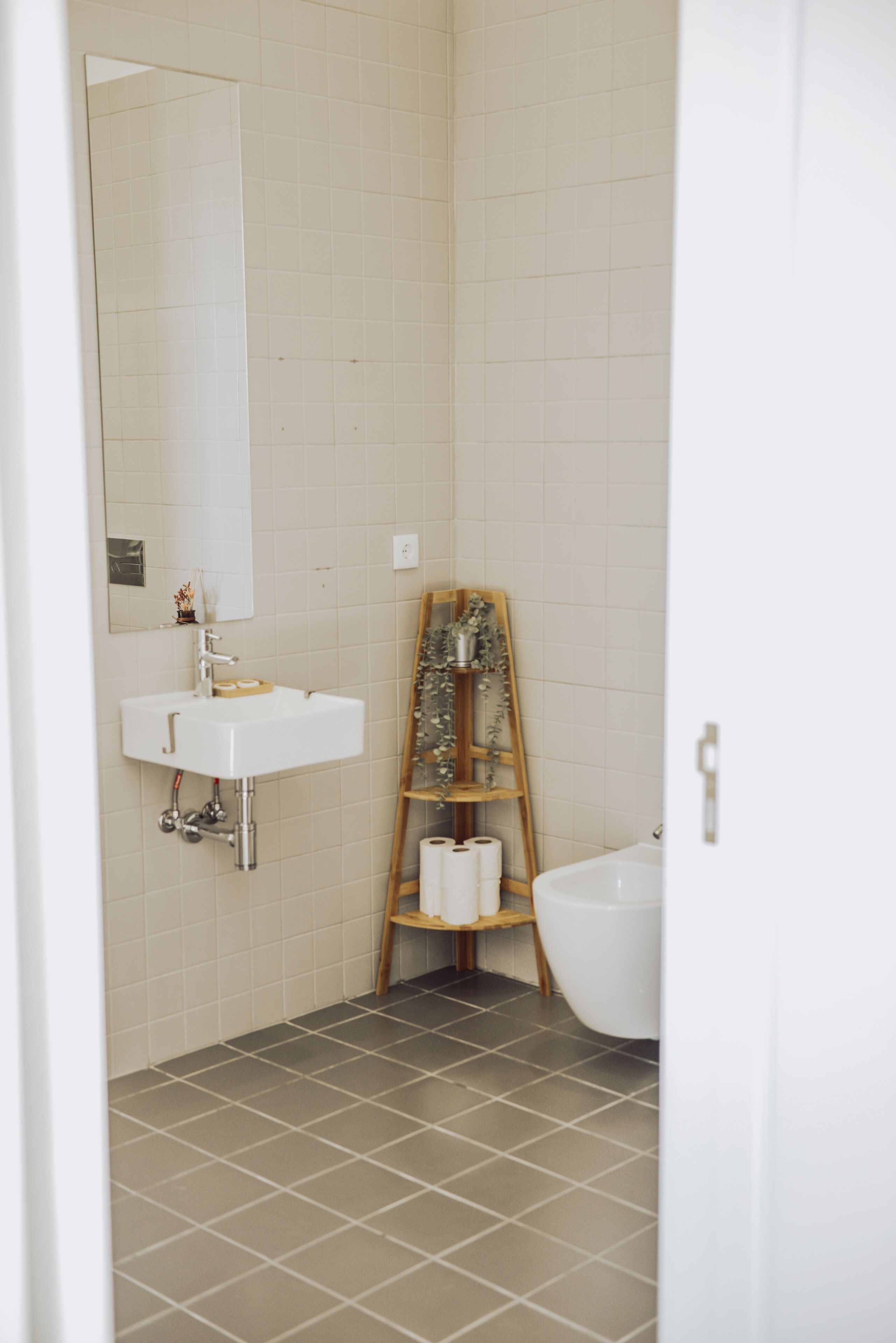 Ein Badezimmer mit einem weißen Waschbecken, einem Spiegel und einem Holzregal mit Toilettenartikeln.