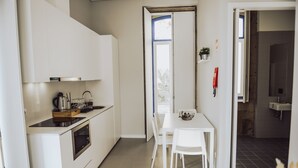 A modern kitchen with white cabinetry, a built-in oven, and a dining area with a white table and chairs.