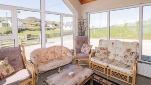 Una habitación con muebles de mimbre, ventanas amplias y vistas al campo.