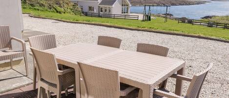 Une terrasse avec une table et des chaises, donnant sur un plan d’eau et une maison.