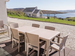 A patio with a table and chairs, overlooking a body of water and a house.