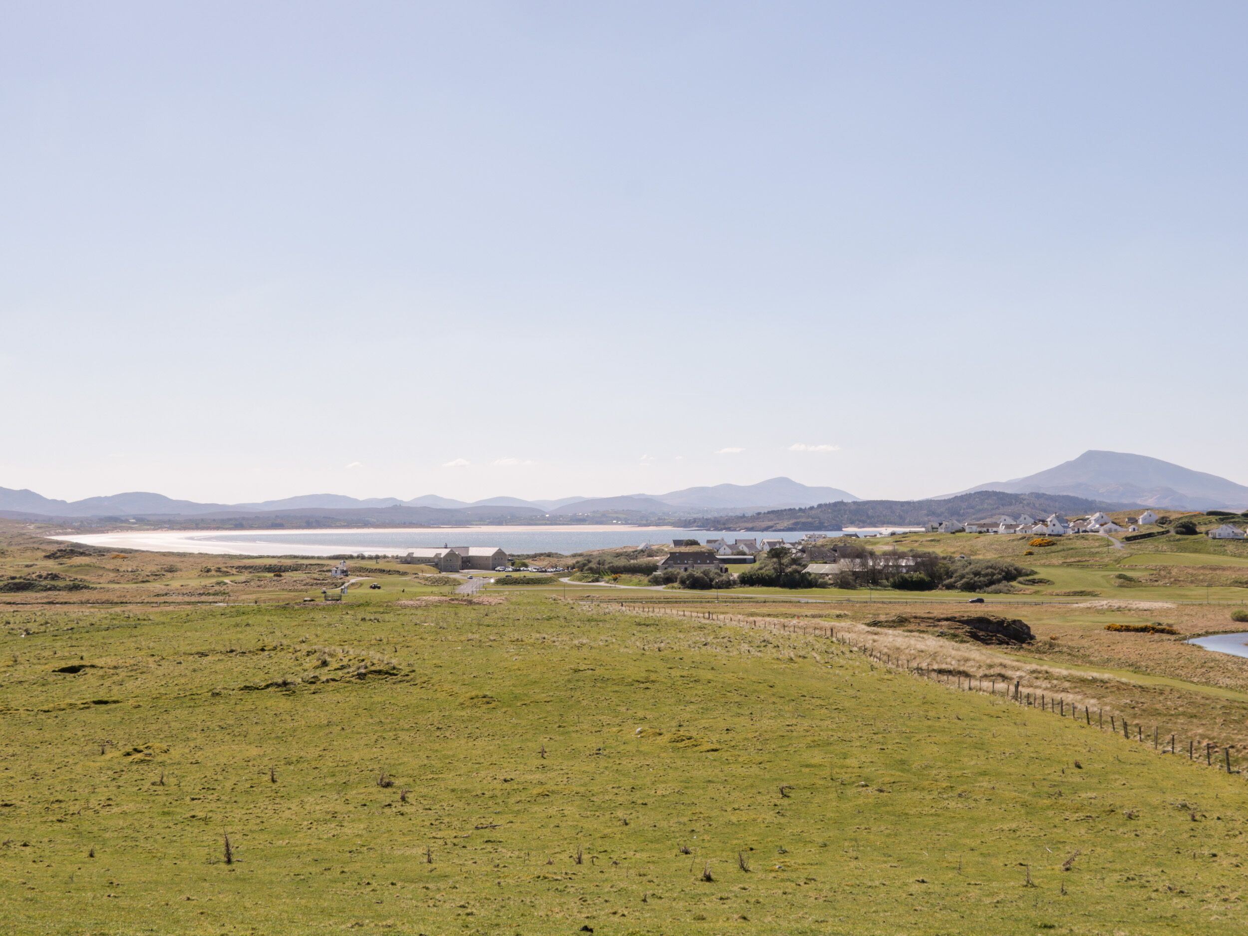 Paisagem rural com céu limpo, um corpo d'água e uma montanha ao longe.