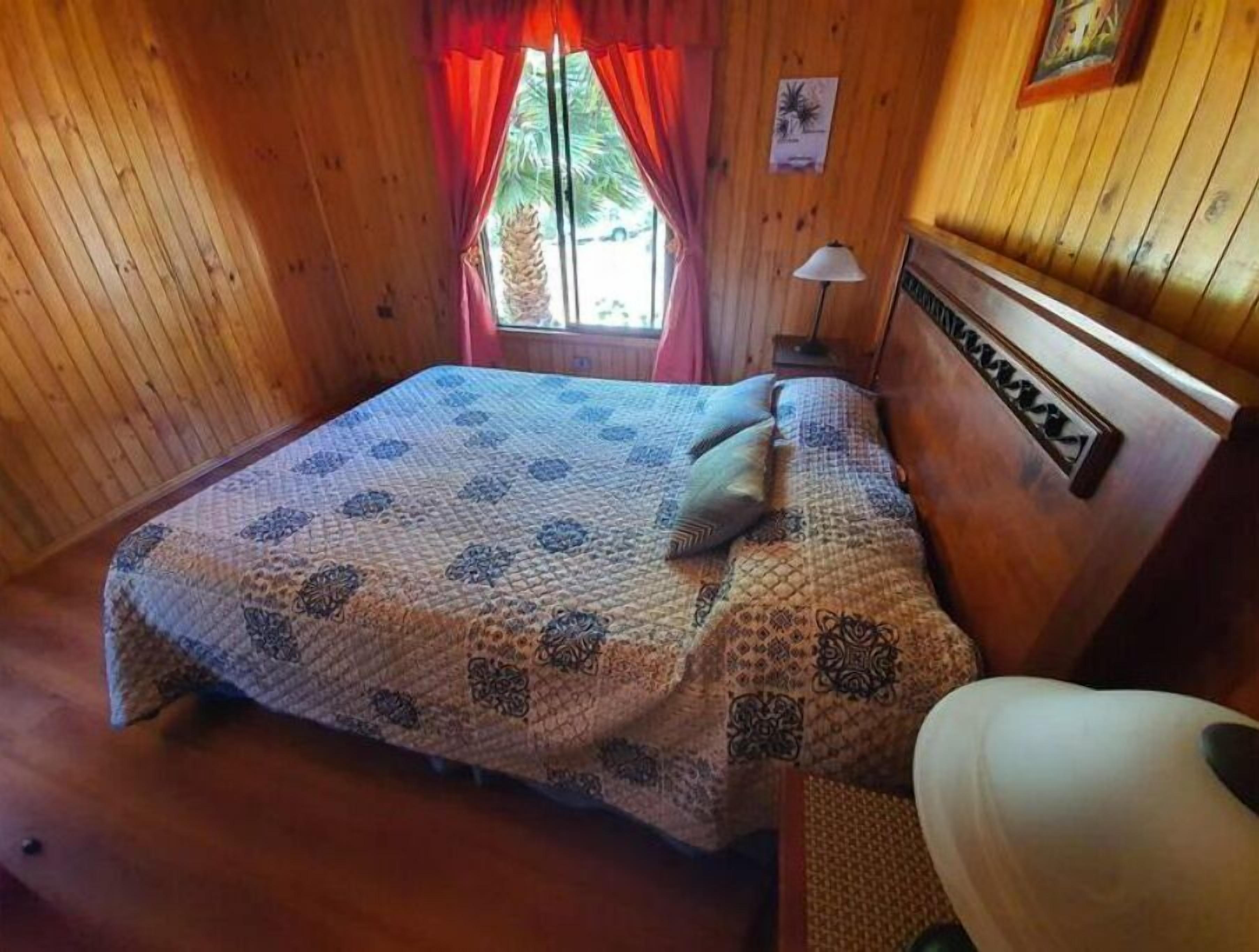 Une pièce en bois avec un lit, une table de chevet et une fenêtre avec des rideaux.