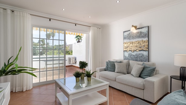 A modern living room with a glass coffee table, a beige sofa, and a large painting on the wall.