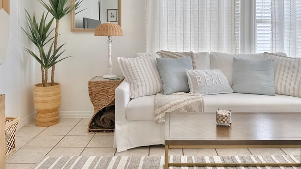 Una sala de estar con un sofá blanco, almohadas a rayas, una mesita de noche tejida y una planta en maceta.