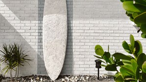 Una tabla de surf blanca apoyada contra una pared de ladrillos blancos, con el texto 'The Coconut' escrito encima.
