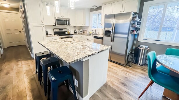 A modern kitchen with white cabinets, stainless steel appliances, a granite island, and blue bar stools. - Quiet Clean Pet Friendly Close to Downtown Sleeps 10 (Colorado Springs)