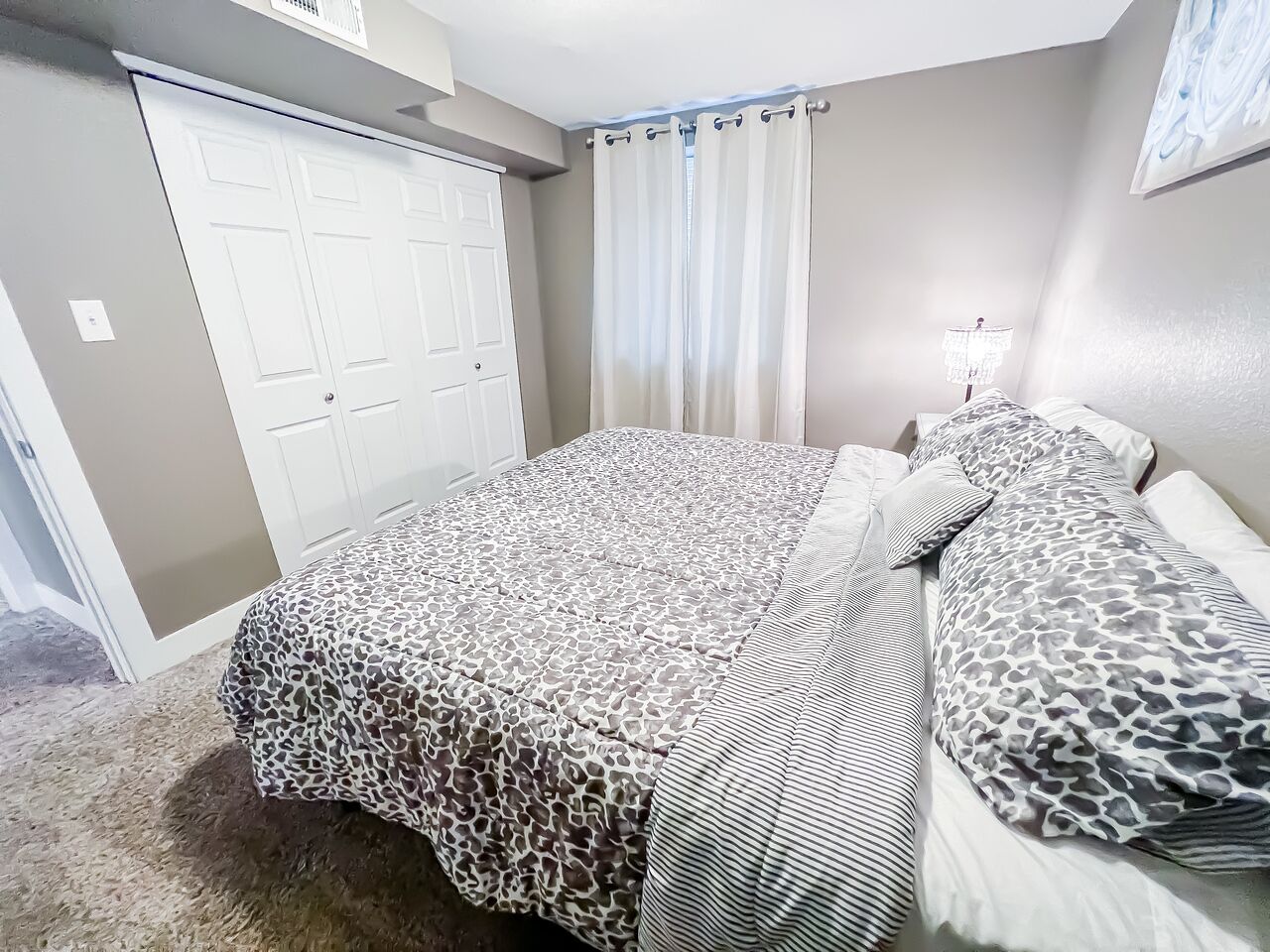 A bedroom with a bed, a nightstand, a lamp, and a door.