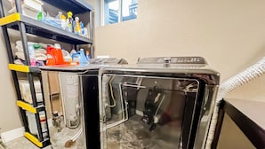 A laundry room with two washing machines, a shelf with cleaning supplies, and a window in the background. - Quiet Clean Pet Friendly Close to Downtown Sleeps 10 (Colorado Springs)