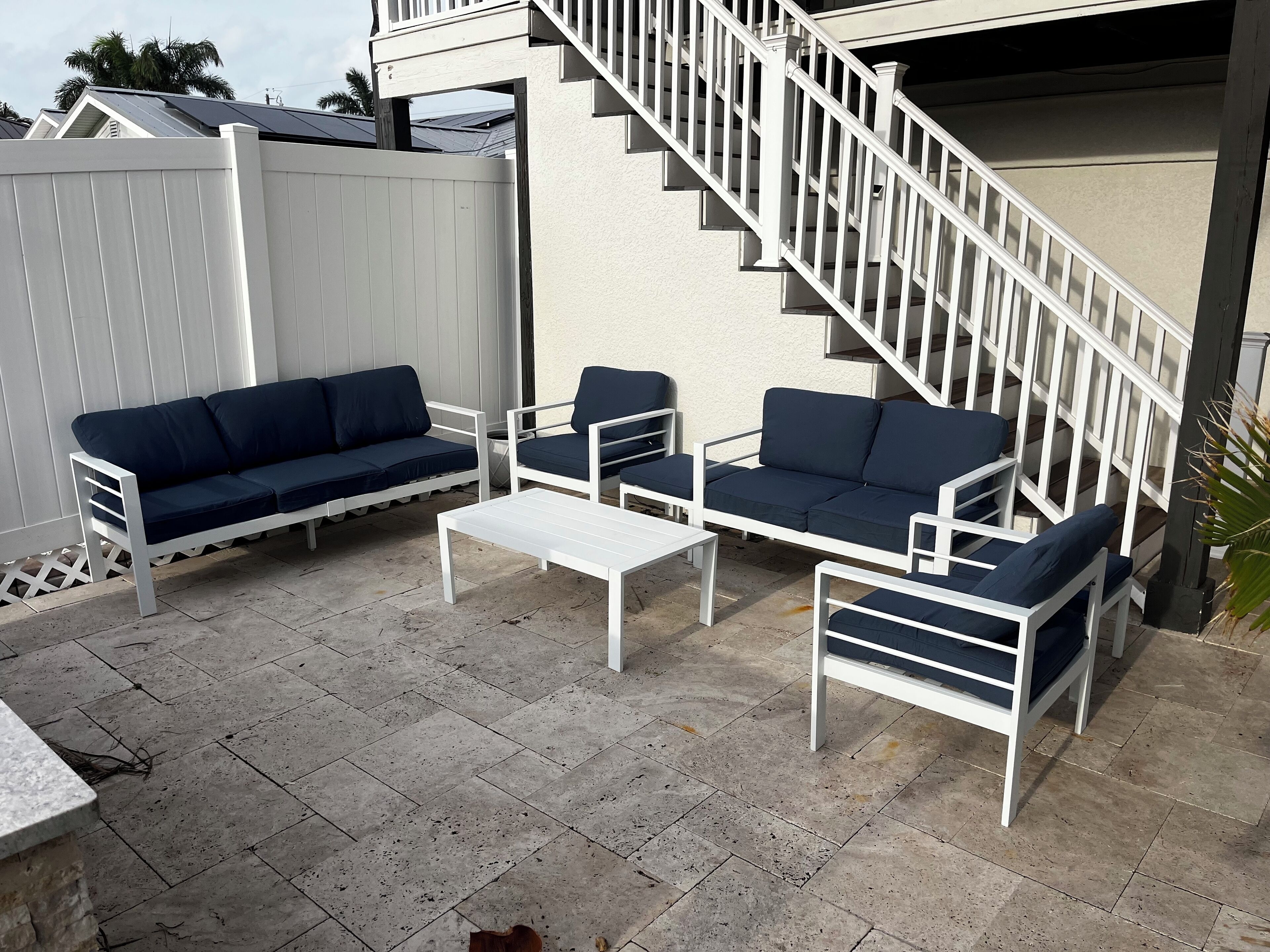 Une terrasse dotée d’un escalier blanc, d’une clôture blanche et de mobilier d’extérieur comprenant un canapé et des fauteuils.