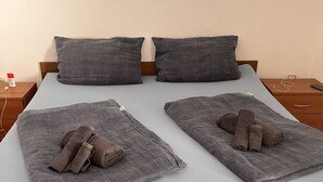 Cama bem arrumada com roupa de cama e toalhas cinzas, cabeceira de madeira e mesa de cabeceira de madeira com um telefone e carregador.