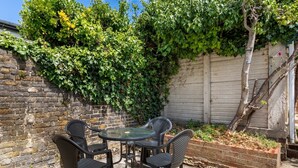 Un patio con una mesa redonda y cuatro sillas, rodeado por un muro de ladrillo y una valla de madera.