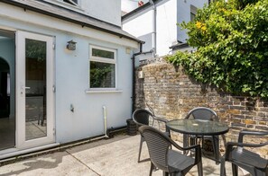 A patio with a table and chairs, a sliding glass door, and a brick wall with greenery. - 2 b&b 40 Percent off Weekly Half Price Monthly (Deal)