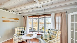 Una habitación acogedora con dos sillones a cuadros, una mesita redonda y un ventanal con cortinas.