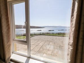 A view from a window overlooking a pebble beach with a wooden fence and distant hills. - Inverbeg Cottage 2 (Downings)