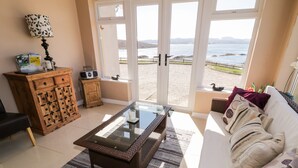 Un soggiorno con un tavolino in vetro, un divano con cuscini decorati, un mobile in legno e vista mare attraverso ampie vetrate.