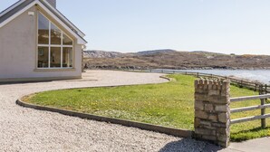 Una casa sulla costa con vialetto sterrato, muro in pietra e vista sul mare e le colline.
