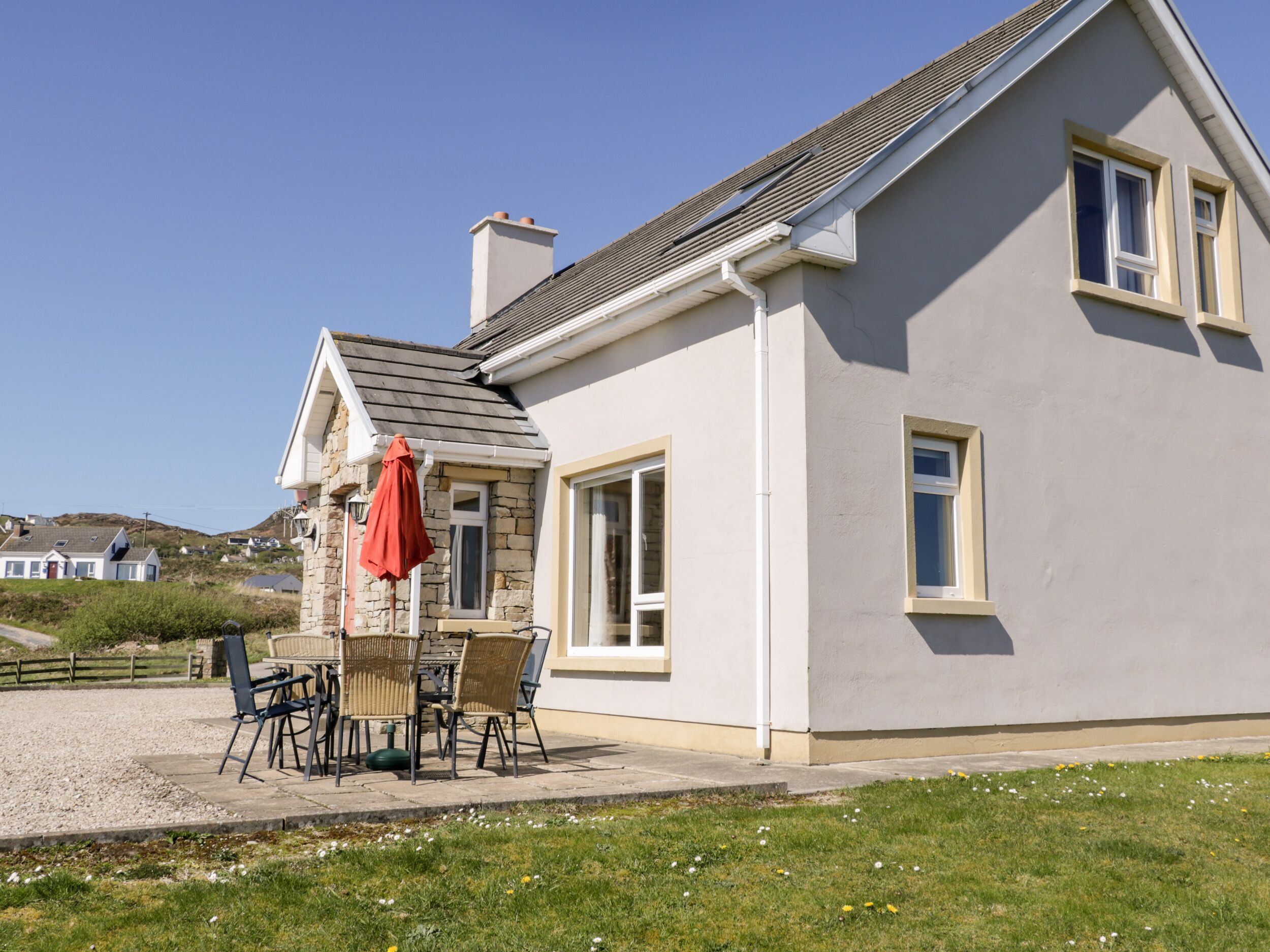 A two-story house with a stone facade, a tiled roof, and a patio with outdoor furniture.
