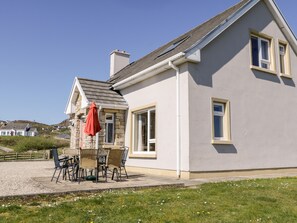 A two-story house with a stone facade, a tiled roof, and a patio with outdoor furniture. - Inverbeg Cottage 2 (Downings)
