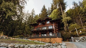A multi-story log cabin with a stone retaining wall and a wooden deck.